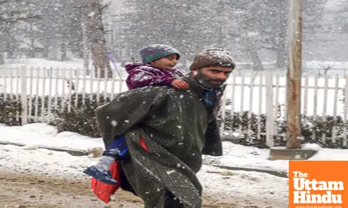 Baramulla: A man carrying a child on his back on a snow-covered road amid heavy snowfall
