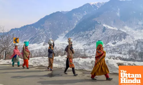 Ganderbal: Women carry water containers on their heads while walking along a snow-covered road