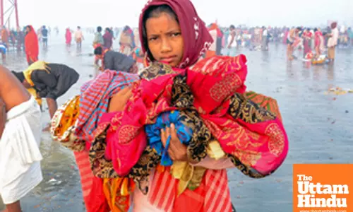 South 24 Parganas: A girl holds onto clothes of her relative during the holy dip at Gangasagar Island