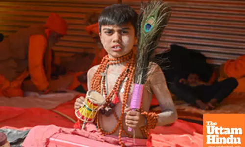 Prayagraj: A child with Pellet drum (Damru) and Peacock feather poses for a photo at the Triveni Sangam